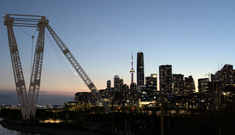The Atlas Crane in Toronto's Biidaasige Park as seen in twilight with the downtown skyline in the background. Venus at the moon are lined up along one of the structure's legs.